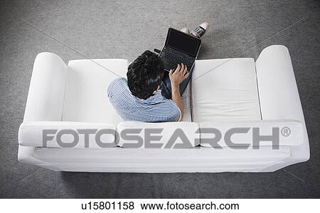 High angle view of a man sitting on a couch working on a laptop View Large Photo Image Stock Photo - High angle view of a man sitting on a couch working on a laptop. Fotosearch