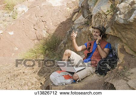 Stock Image - Hiker sitting on a rock and talking on a mobile phone. Fotosearch