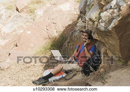 Stock Photo - Hiker sitting on a rock and talking on a mobile phone. Fotosearch