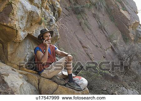 Stock Photo - Hiker sitting on a rock and talking on a mobile phone. Fotosearch
