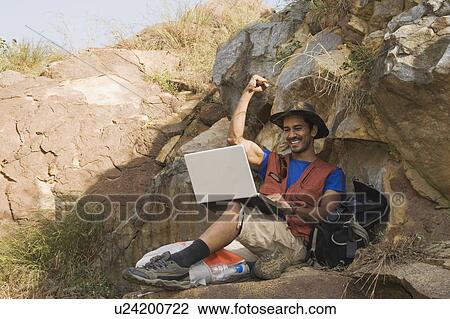 Hiker sitting on a rock and using a laptop View Large Photo Image Stock Image - Hiker sitting on a rock and using a laptop. Fotosearch