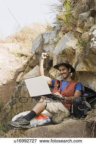 Hiker sitting on a rock and using a laptop View Large Photo Image Stock Photo - Hiker sitting on a rock and using a laptop. Fotosearch