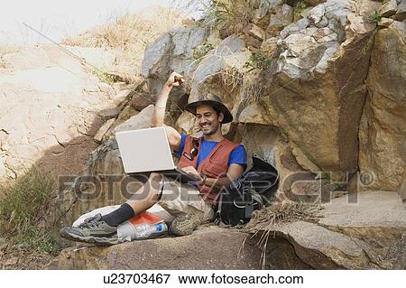 Stock Photo - Hiker sitting on a rock and using a laptop. Fotosearch