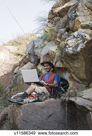 Hiker sitting on rocks and using a laptop View Large Photo Image Stock Photo - Hiker sitting on rocks and using a laptop. Fotosearch