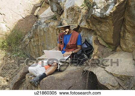 Stock Photography - Hiker sitting on rocks and using a laptop. Fotosearch