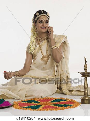 Picture - Indian woman in traditional clothing making rangoli and talking on a mobile phone. Fotosearch