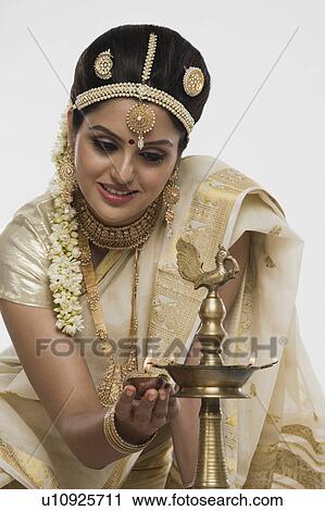 Stock Image - Indian woman in traditional clothing lighting an oil lamp. Fotosearch