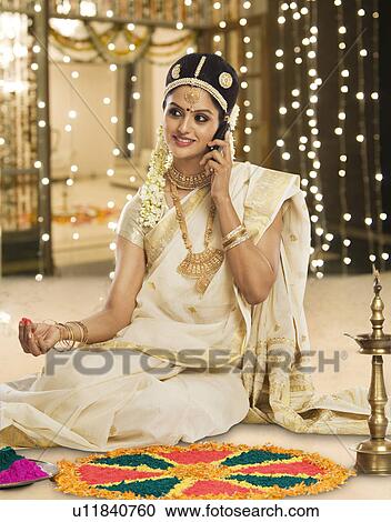 Stock Image - Indian woman in traditional clothing making rangoli and talking on a mobile phone. Fotosearch