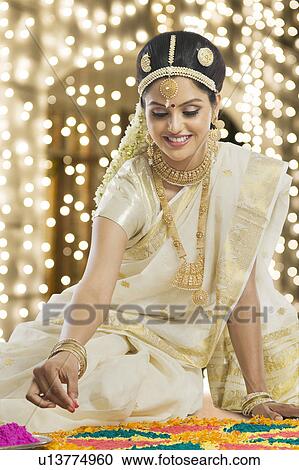 Stock Image - Indian woman in traditional clothing making rangoli at Durga festival. Fotosearch