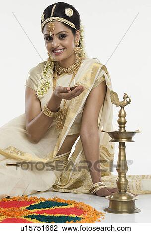 Stock Image - Indian woman in traditional clothing lighting an oil lamp. Fotosearch
