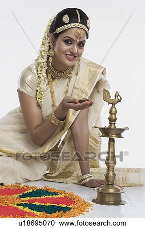 Stock Image - Indian woman in traditional clothing lighting an oil lamp. Fotosearch