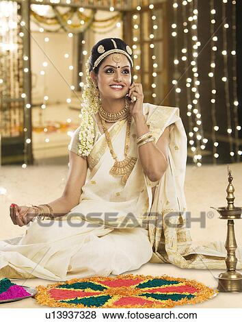 Stock Photo - Indian woman in traditional clothing making rangoli and talking on a mobile phone. Fotosearch