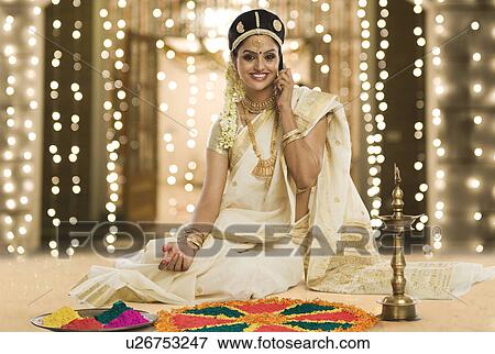 Stock Photo - Indian woman in traditional clothing making rangoli and talking on a mobile phone. Fotosearch