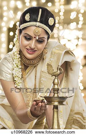 Stock Photograph - Indian woman in traditional clothing lighting an oil lamp. Fotosearch