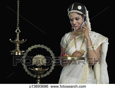 Indian woman in traditional clothing holding religious offering and talking on a mobile phone View Large Photo Image Stock Photograph - Indian woman in traditional clothing holding religious offering and talking on a mobile phone. Fotosearch