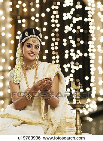 Stock Photograph - Indian woman in traditional clothing lighting an oil lamp. Fotosearch