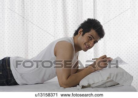 Stock Image - Man doing paperwork on the bed. Fotosearch