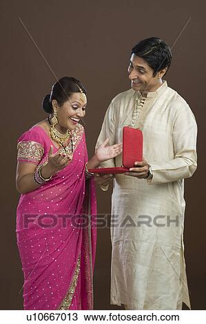 Stock Image - Man giving a jewelry box to his wife in present. Fotosearch