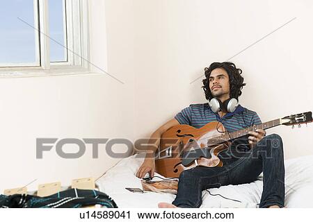Stock Image - Man holding a guitar in the bedroom. Fotosearch
