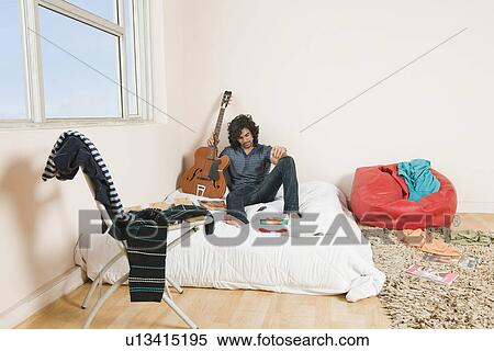 Stock Photography - Man holding a guitar in the bedroom. Fotosearch