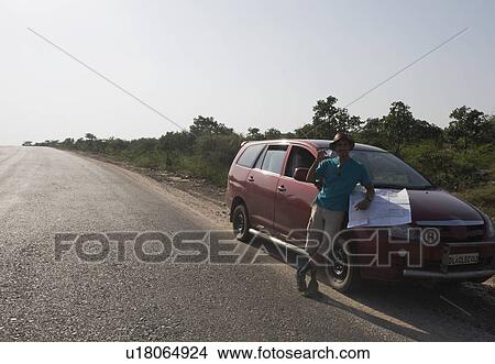 Picture - Man holding a map on a car hood. Fotosearch