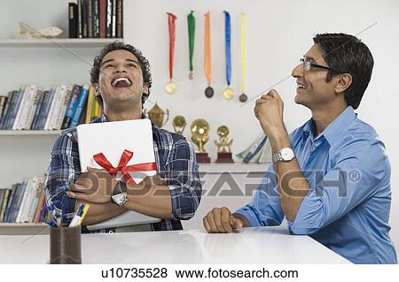Stock Photo - Man laughing and hugging a laptop gifted by his father. Fotosearch