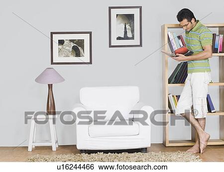 Stock Photograph - Man leaning against a bookshelf and reading a book. Fotosearch