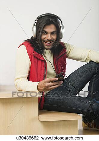 Stock Image - Man listening to an MP3 player on a staircase. Fotosearch