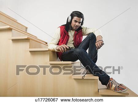 Man listening to an MP3 player on a staircase View Large Photo Image Stock Photo - Man listening to an MP3 player on a staircase. Fotosearch