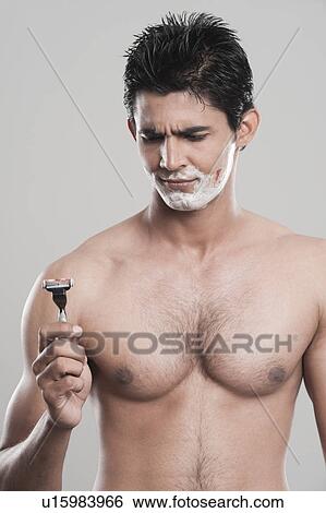 Man looking at razor with a shaving cut on face View Large Photo Image Stock Photograph - Man looking at razor with a shaving cut on face. Fotosearch