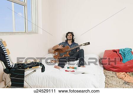 Stock Image - Man playing a guitar in the bedroom. Fotosearch
