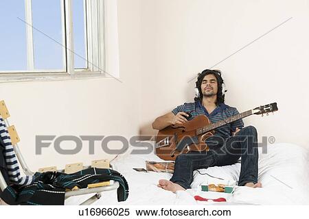 Stock Photography - Man playing a guitar in the bedroom. Fotosearch