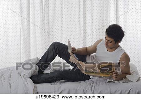 Stock Photo - Man reading a newspaper on the bed. Fotosearch