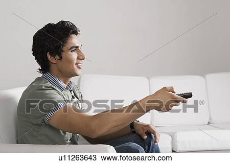 Stock Image - Man sitting on a couch watching television. Fotosearch