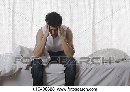 Stock Photo - Man sitting on the bed and holding head. Fotosearch