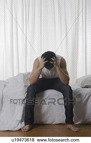 Stock Photo - Man sitting on the bed and holding head. Fotosearch