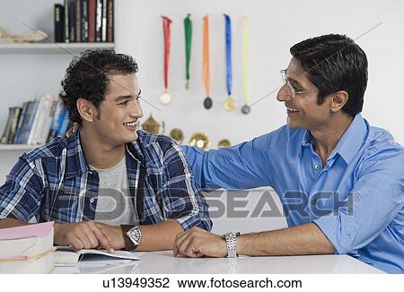 Stock Image - Man smiling at his son studying. Fotosearch