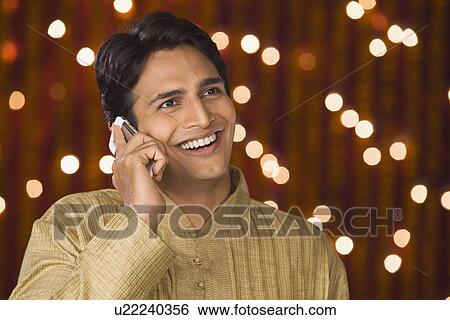 Stock Photograph - Man talking on a mobile phone in front of Diwali decoration. Fotosearch