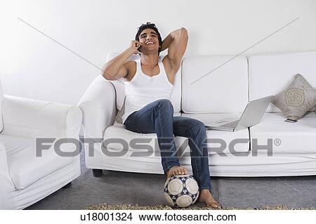 Picture - Man talking on a mobile phone on a couch. Fotosearch