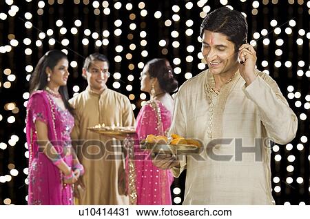 Stock Image - Man talking on a mobile phone with his family in the background. Fotosearch