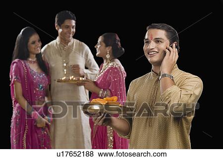 Stock Photo - Man talking on a mobile phone with his family in the background. Fotosearch