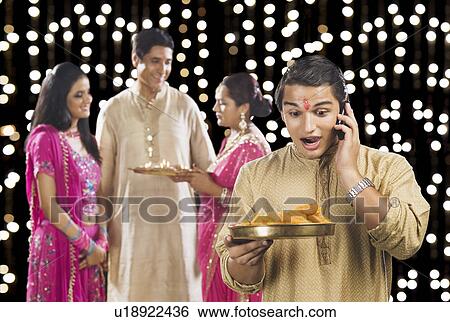 Stock Photograph - Man talking on a mobile phone with his family in the background. Fotosearch