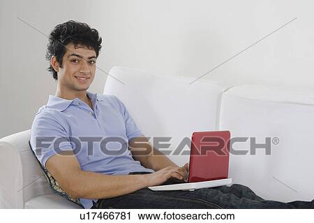 Stock Image - Man using a laptop on a couch. Fotosearch