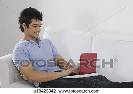 Stock Image - Man using a laptop on a couch. Fotosearch