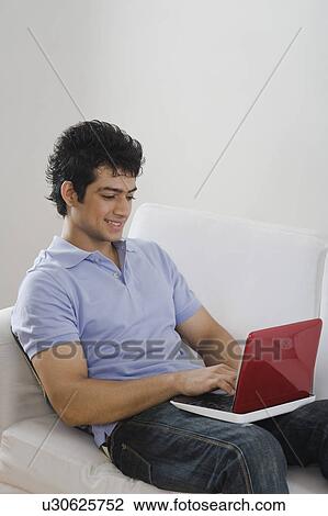 Stock Image - Man using a laptop on a couch. Fotosearch