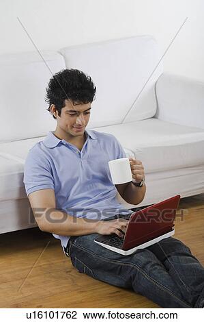 Stock Image - Man using a laptop with a cup of coffee on the floor. Fotosearch