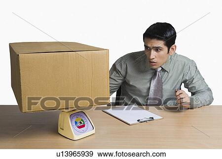 Stock Photo - Man weighing a cardboard box and recording data. Fotosearch