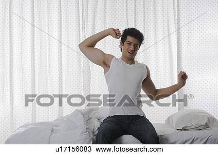 Stock Image - Man yawning and stretching on the bed. Fotosearch