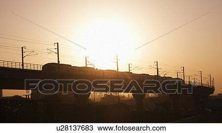 Stock Image - Metro train on elevated tracks at sunset, Delhi, India. Fotosearch