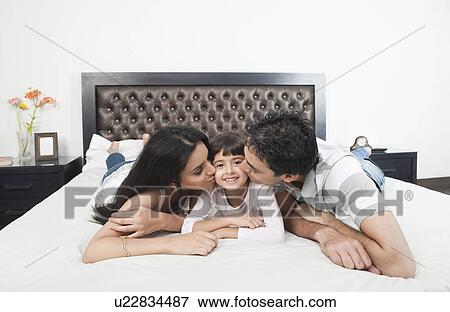 Stock Photo - Parents kissing their daughter. Fotosearch